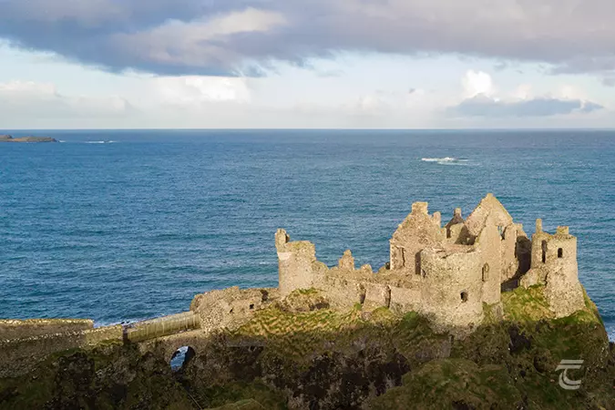 Light shines on Dunluce Castle with the Atlantic Ocean beyond. The Skerries Islands are visible in the left background.