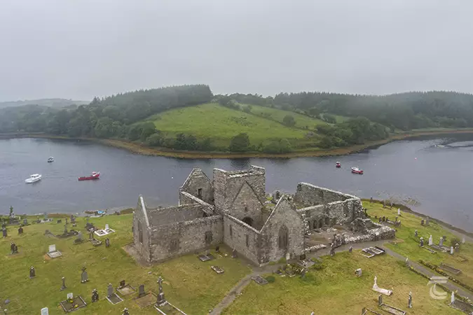 A high aerial view of Burrishoole Abbey, Mayo on a misty day. The abbey is surrounded by a graveyard, and with the estuary behind it.