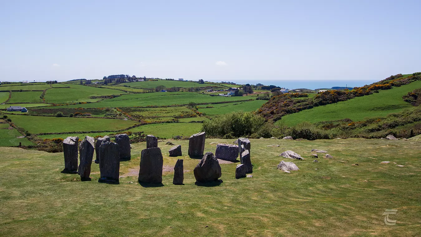 17 tall stones stand in circular alignment among green fields