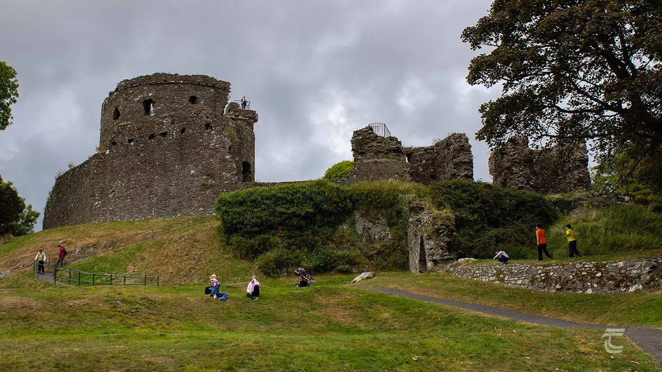 The keep of Dundrum Castle from below with visitors sitting in the grass.
