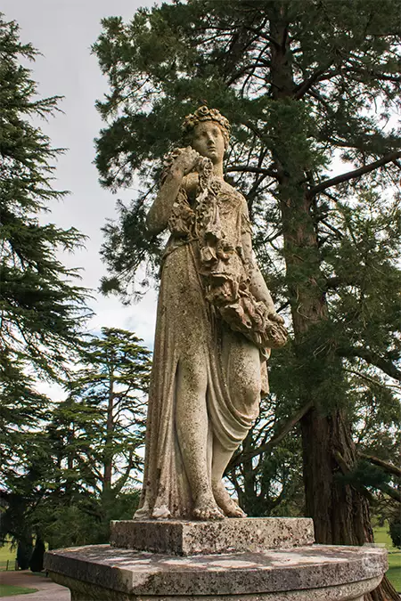 An outdoor stone statue of a woman stands on a plinth