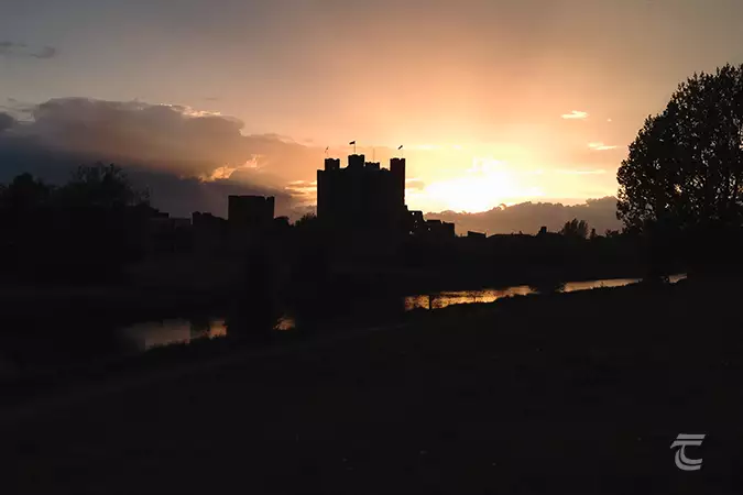 The outline of Trim Castle at dusk, with the last rays of sunshine cvisible on the horizon